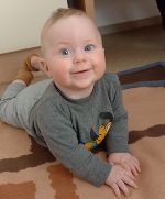 Das Bild zeigt ein männliches Baby, das in die Kamera lacht.