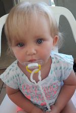 Das Foto zeigt ein weibliches Baby, dass einen Schnuller im Mund hat und in die Kamera schaut.