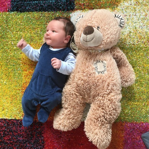 Ein Baby liegt neben einem großen Teddybär auf dem Boden.