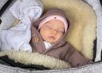 Ein Baby liegt schlafend in einem Kinderwagen. Es trägt eine braune Jacke und eine Haube. Ein Baby liegt schlafend in einem Kinderwagen. Es trägt eine braune Jacke und eine Haube.