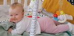 Das Bild zeigt ein weibliches Baby, das am Bauch liegt und in die Kamera lächelt. 