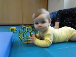 Baby liegt am Bauch und hält ein Spielzeug in der Hand.