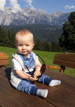 Ein ca. 6 Monate alter Junge sitzt auf einem Tisch. Im Hintergrund sieht man die Berge.
